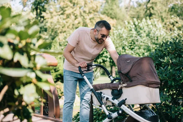 Souriant père regardant la voiture de bébé dans le parc — Photo de stock