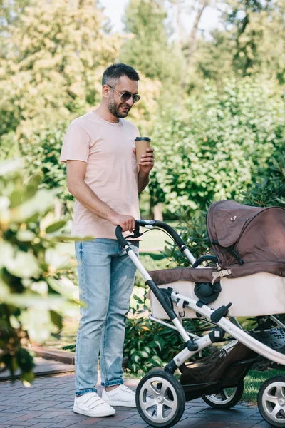 Pai andando com carrinho de bebê no parque e segurando copo de café descartável — Fotografia de Stock