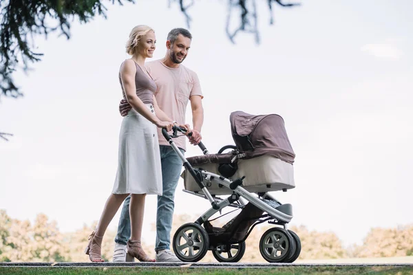 Parents heureux marchant avec la voiture de bébé dans le parc le week-end — Photo de stock