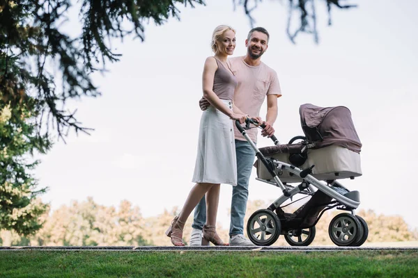 Счастливые родители гуляющие с детской коляской в парке — стоковое фото
