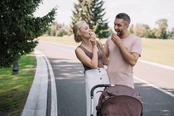Happy parents eating ice cream near baby carriage in park — Stock Photo