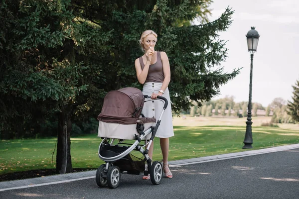 Mãe andando com carrinho de bebê e comer sorvete no parque — Fotografia de Stock