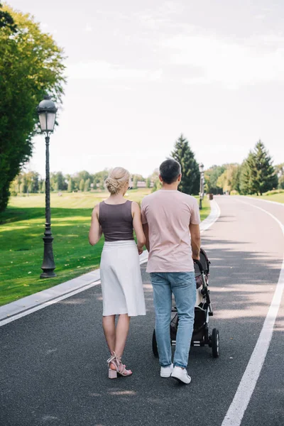 Rear view of parents walking with baby carriage on road in park — Stock Photo