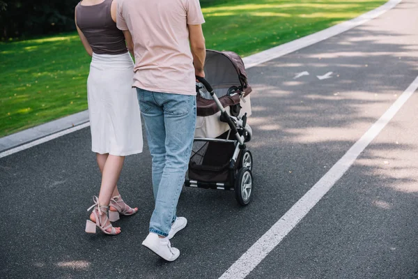 Обрезанное изображение родителей, идущих с детской коляской по дороге в парке — стоковое фото
