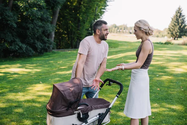Side view of parents quarreling near baby carriage in park — Stock Photo