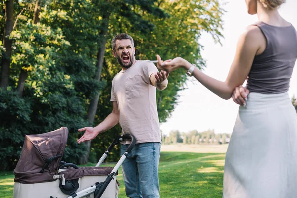 Cropped image of mother smoking cigarette near baby carriage in park, father yelling at her — Stock Photo
