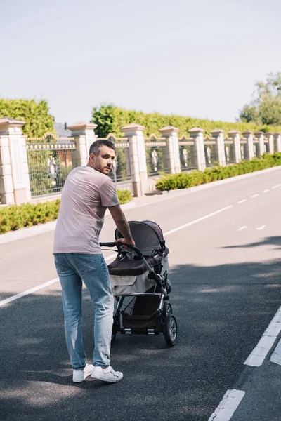 Vue arrière du père marchant avec la voiture de bébé dans le parc — Photo de stock