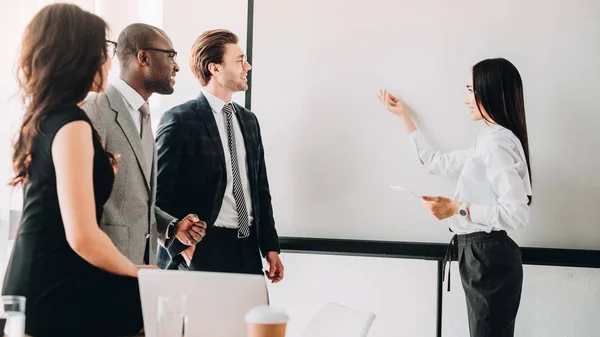 Empresários multiculturais olhando para o conselho branco vazio durante reunião de negócios no escritório — Fotografia de Stock