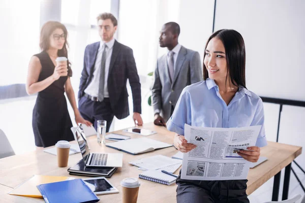 Selective focus of asian businesswoman with newspaper and colleagues behind in office — Stock Photo