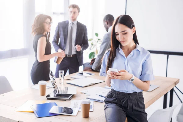 Selective focus of asian businesswoman using smartphone and colleagues behind in office — Stock Photo