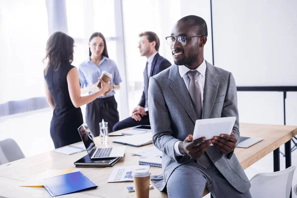 Foco seletivo de sorrir empresário afro-americano com café para ir e colegas no local de trabalho no escritório — Fotografia de Stock