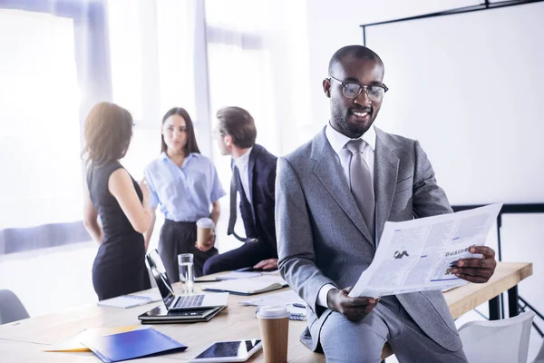 Selective focus of african american businessman reading newspaper and colleagues at workplace in office — Stock Photo