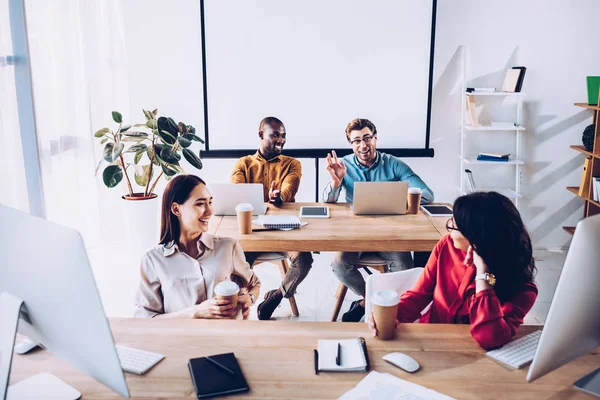 Sonriente interracial jóvenes empresarios hablando durante el trabajo en la oficina - foto de stock