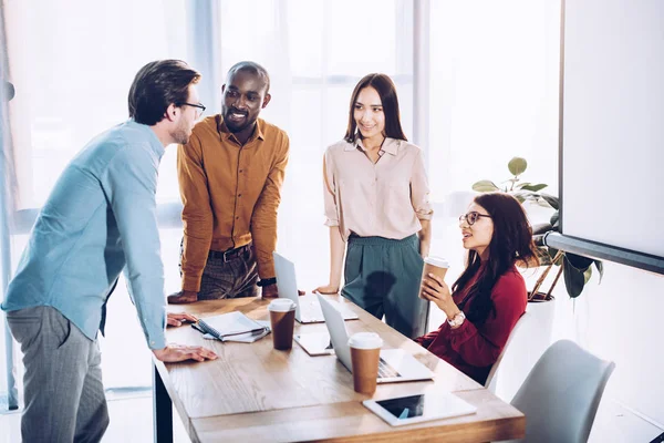 Interracial group of business colleagues discussing work during coffee break at workplace in office — Stock Photo