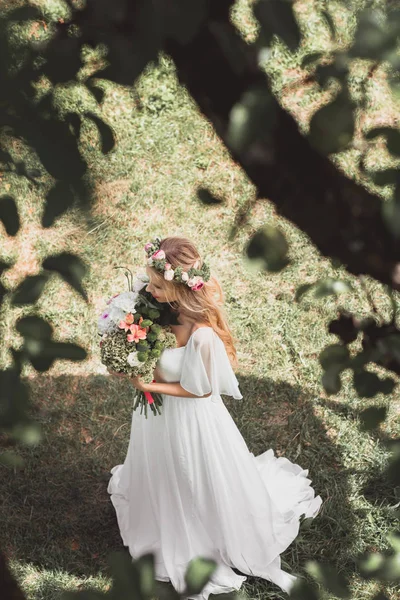 Vista ad alto angolo di bella giovane sposa che tiene mazzo di fiori nel parco — Foto stock