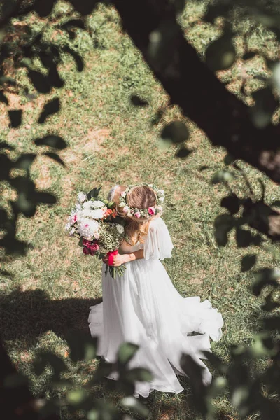 Selective focus of beautiful young bride holding bouquet of flowers in park — Stock Photo