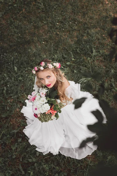 Overhead view of beautiful young bride holding bouquet of flowers and looking at camera — Stock Photo