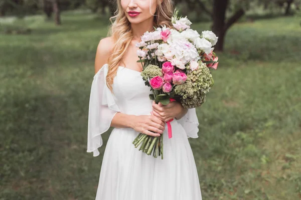 Plan recadré de belle jeune mariée tendre tenant bouquet de mariage en plein air — Photo de stock