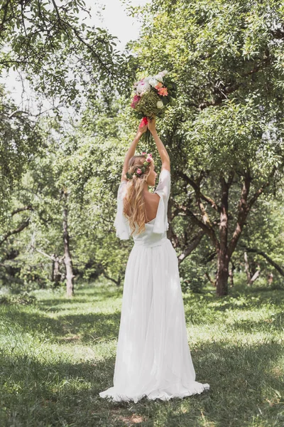 Vista posteriore della bella giovane sposa in abito da sposa lancio bouquet nel parco — Foto stock