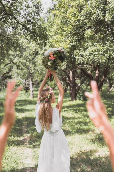 Enfoque selectivo de la novia joven lanzando ramo de boda en el parque - foto de stock