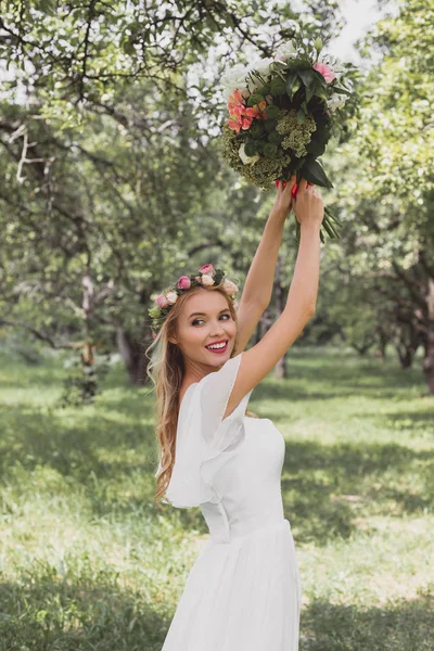 Красива усміхнена молода наречена кидає весільний букет в парк — стокове фото