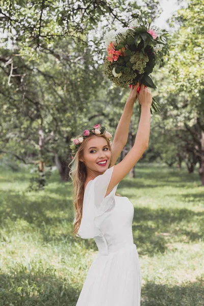 Bela sorridente jovem noiva jogando buquê de casamento no parque — Fotografia de Stock