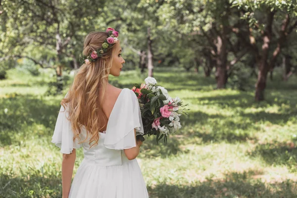 Vue arrière de tendre jeune mariée tenant bouquet de mariage et marche dans le parc — Photo de stock