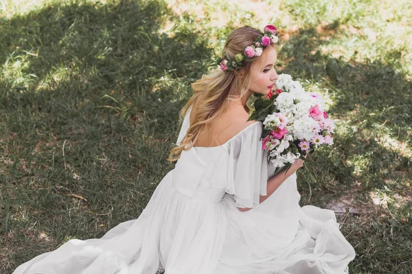Blick aus der Vogelperspektive auf die schöne junge Braut im Brautkleid, die einen Blumenstrauß hält und im Park wegschaut — Stockfoto