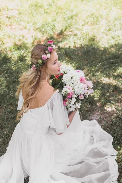 Vista ad alto angolo di bella giovane sposa in abito da sposa con mazzo di fiori in parco — Foto stock