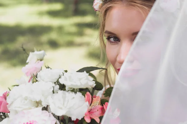 Bela noiva jovem em véu segurando buquê de flores e olhando para a câmera — Fotografia de Stock