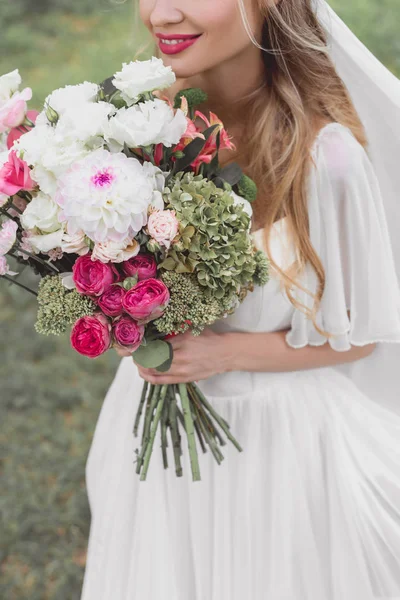 Tiro cortado de sorrir jovem noiva segurando buquê de flores ao ar livre — Fotografia de Stock