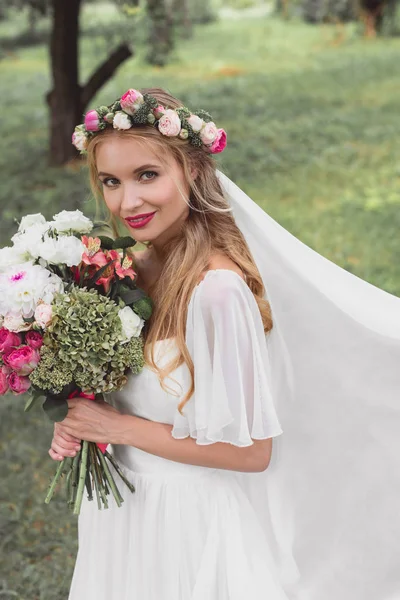 High angle view of beautiful young bride holding wedding bouquet and smiling at camera outdoors — Stock Photo