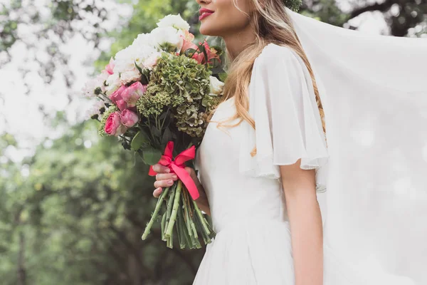 Schnappschuss einer jungen Braut in Brautkleid und Schleier mit schönem Blumenstrauß — Stockfoto