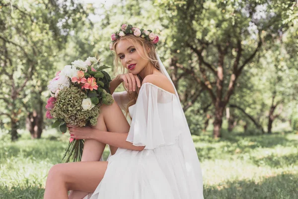 Hermosa novia rubia celebración de ramo de bodas y mirando a la cámara al aire libre - foto de stock