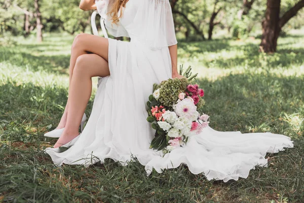 Schnappschuss einer Braut im Brautkleid, die auf einem Stuhl sitzt und einen Blumenstrauß im Freien hält — Stockfoto