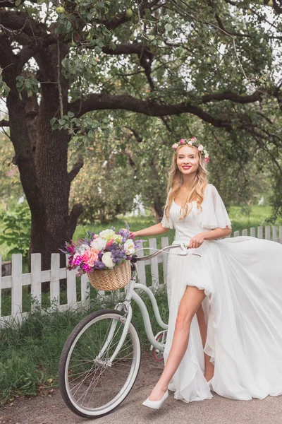 Belle jeune mariée marchant à vélo et souriant à la caméra — Photo de stock