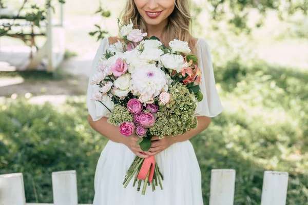 Cropped shot of happy blonde bride holding beautiful wedding bouquet outdoors — Stock Photo