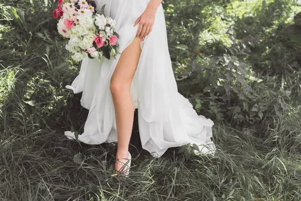 Low section of young bride in wedding dress holding bouquet of flowers in garden — Stock Photo