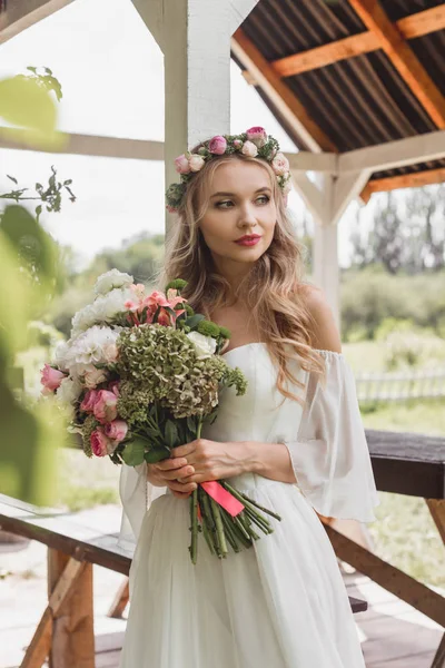 Belle jeune mariée coûteuse tenant bouquet de fleurs et détournant les yeux — Photo de stock