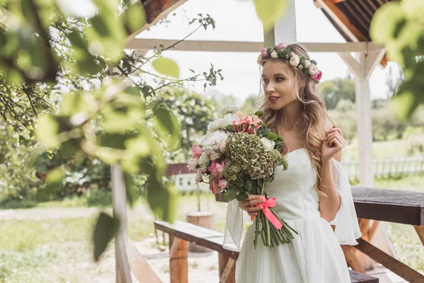 Schöne zarte junge Braut hält Hochzeitsstrauß und schaut weg — Stockfoto