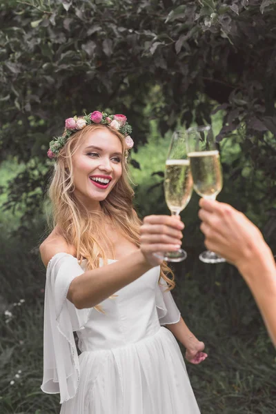 Vue partielle de jeune mariée heureuse cliquetis verres de vin avec quelqu'un dans le parc — Photo de stock