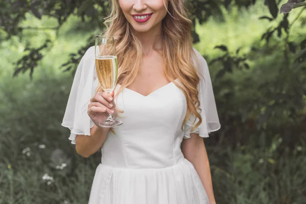 Ritagliato colpo di sorridente giovane sposa bionda in possesso di un bicchiere di vino all'aperto — Foto stock