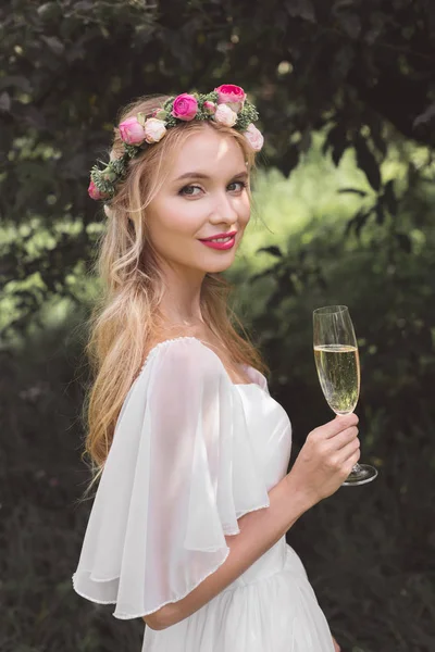 Bela jovem noiva segurando copo de vinho e sorrindo para a câmera ao ar livre — Fotografia de Stock