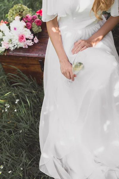 Обрезанный снимок невесты, держащей бокал шампанского и сидящей на винтажной груди — стоковое фото