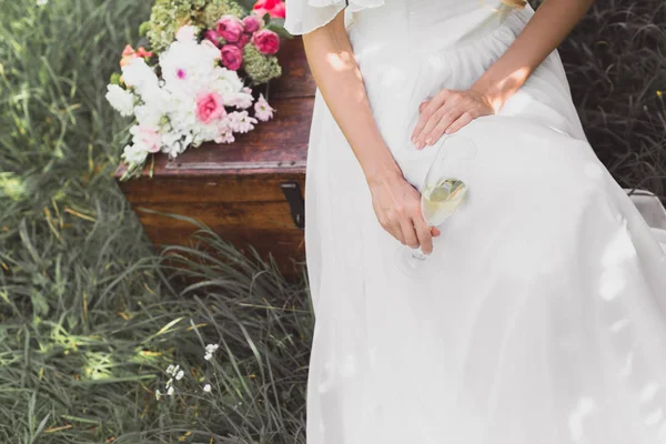 Tiro recortado de novia sosteniendo vaso de vino y sentado en el pecho vintage - foto de stock