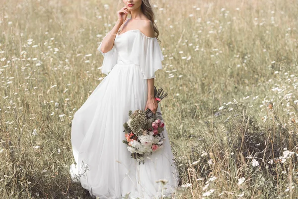 Cropped shot of young bride in wedding dress holding bouquet of flowers outdoors — Stock Photo