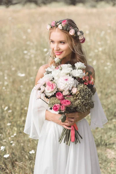 Bella sorridente giovane sposa tenendo bouquet da sposa e guardando lontano all'aperto — Foto stock