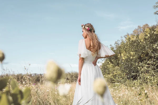 Vista trasera de hermosa novia rubia joven caminando en hermoso campo - foto de stock