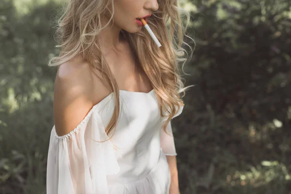 Cropped shot of young blonde woman in white dress smoking cigarette outdoors — Stock Photo