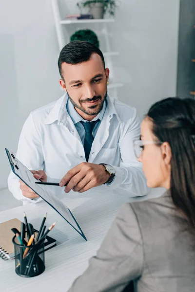 Cheerful doctor pointing on insurance claim form to patient in clinic — Stock Photo